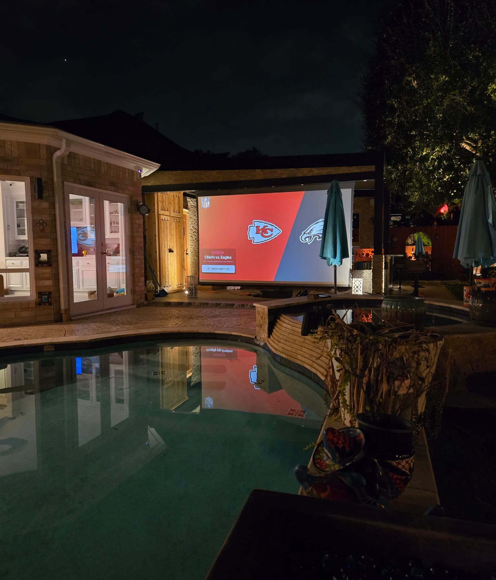 Backyard pool at night with a large outdoor projection screen