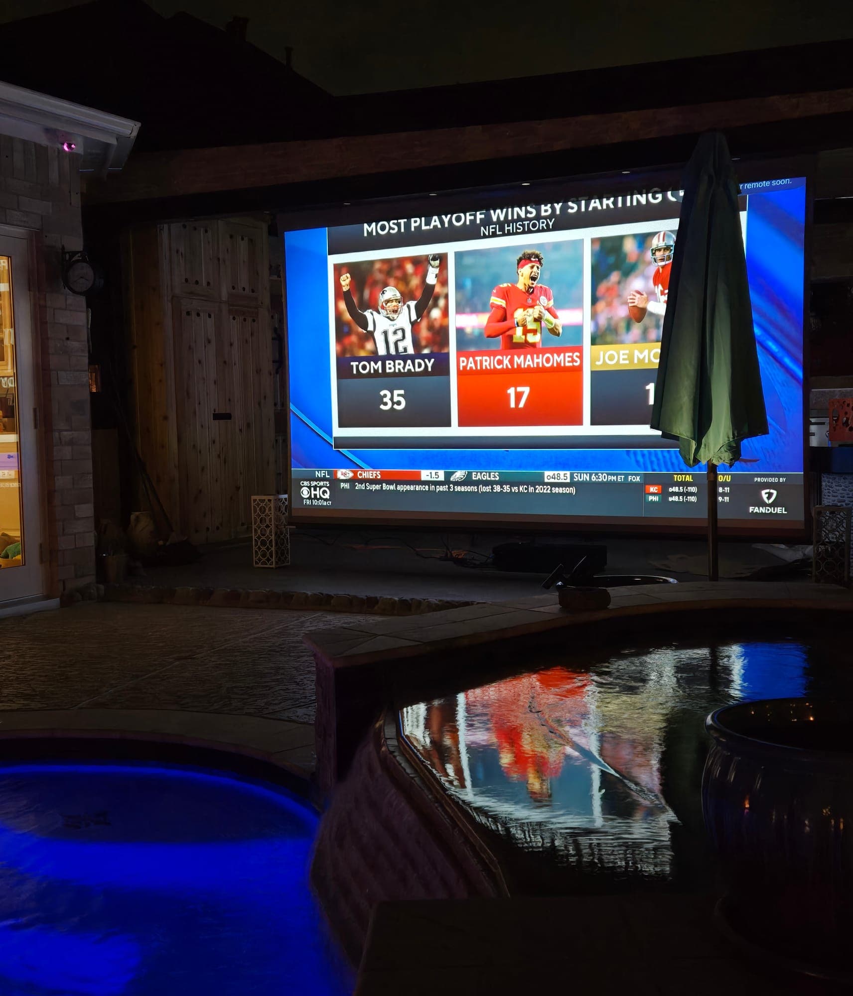Outdoor projector screen by a pool showing a football broadcast
